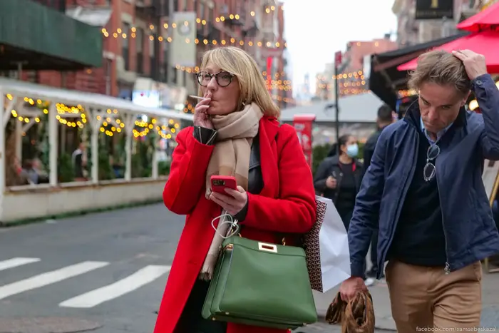 a woman walks through Manhattan in a red coat smoking a cigarette
